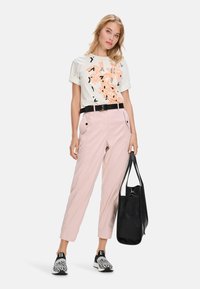 Light-colored cotton t-shirt with orange and black graphic print, paired with pink high-waisted tapered pants, black belt, and black tote bag.