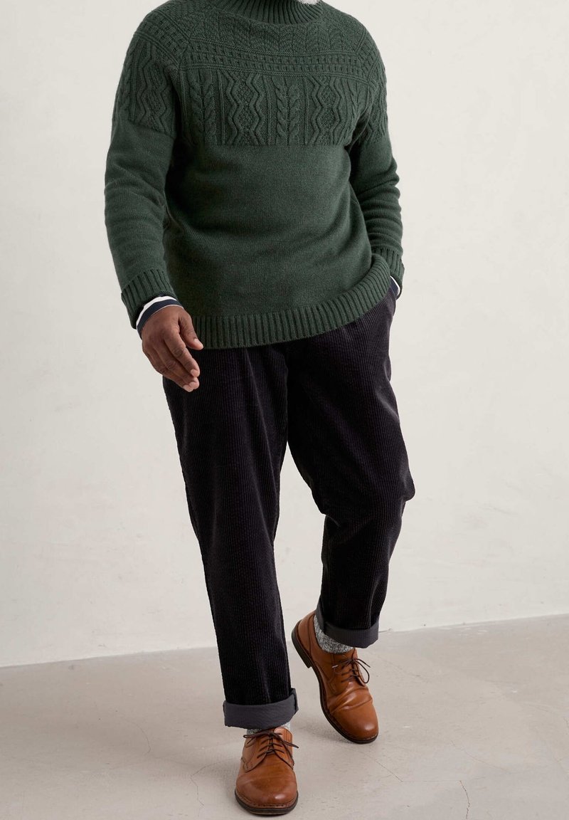Dunkelgrüner Strickpullover mit strukturiertem Muster, beiger Kragenhemd, dunkle Cordhosen und braune Leder Schuhe, die eine lässige Passform zeigen.