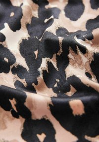 Tissu imprimé léopard présentant une texture lisse. Le motif combine des taches noires sur un fond beige clair avec des variations subtiles de teintes.