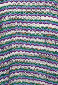 Wielokolorowa dzianina w zygzaki z powtarzającymi się falistymi wzorami w fioletowych, zielonych, niebieskich, białych, pomarańczowych i czarnych nitkach.
