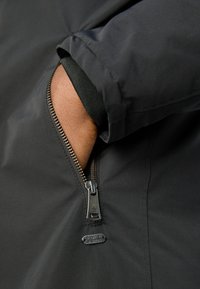 Black jacket featuring a zippered pocket, textured cuff, and a Scotch & Soda logo tag. The material appears smooth and sturdy.