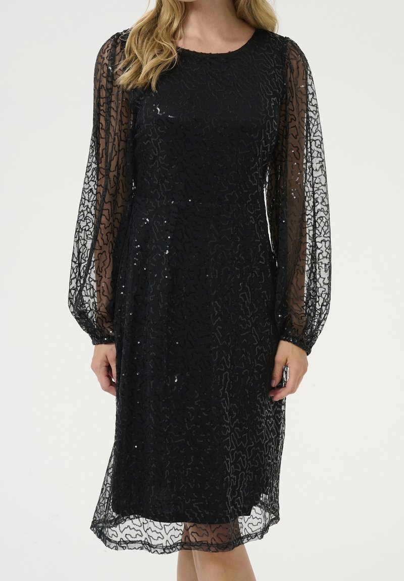 Robe noire avec manches longues transparentes, corsage cintré et motif texturé avec des sequins sur toute la surface. Ourlet à hauteur des genoux.