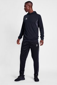 Felpa sportiva nera con accenti grigi, abbinata a pantaloni da jogging neri con un motivo a chevron laterale. Il materiale sembra liscio e leggero.