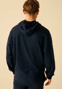 Granatowy hoodie z kieszenią kangurką i kapturem ze sznurkiem. Miękka tkanina, ściśnięte mankiety i dół, pokazany z tyłu.