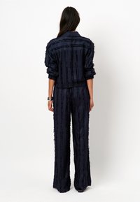 Marineblauwe twee-delige outfit met een getextureerde blazer en wijde broek met verticale strepen en onafgewerkte randen.