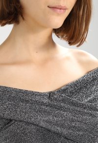 Top nero off-shoulder realizzato in materiale testurizzato e lucente; presenta un design drappeggiato e una forma aderente che accentua il décolleté.