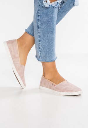 Lys pink canvas slip-on sko med hvide såler, prydet med stikninger og et lille logo, parret med slidte blå jeans.