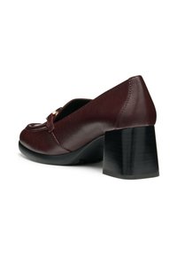 Zapato de tacón de cuero burdeos con punta redonda, que presenta un tacón grueso negro y detalles dorados en la parte delantera. Textura suave.