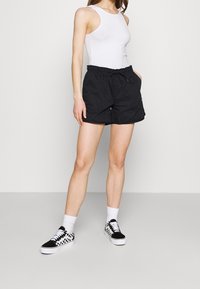 Černé šortky na stažení s bočními kapsami, vyrobené z lehké tkaniny, spárované s jednoduchým bílým tílkem a černobílými kostkovanými teniskami.