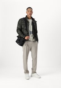 Dark green, lightweight jacket with a collar and front pockets, grey patterned sweater underneath, light grey pants, and white sneakers.