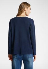 Suéter de manga larga azul marino con cuello redondo y dobladillo acanalado, que muestra un pequeño logo decorativo en la parte de atrás.