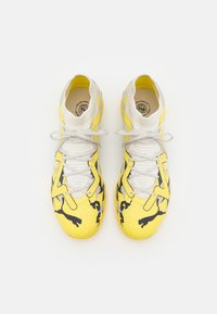 Žluté a černé sportovní boty s texturovaným povrchem, s pleteným límcem, bílými tkaničkami a logem na boku.