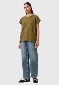 Olivgrünes T-Shirt mit kurzen Ärmeln im lockeren Schnitt, kombiniert mit hellblauen, hoch taillierten, weiten Jeans und schwarzen Ballerinas.
