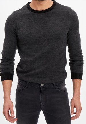 Homme portant un pull ajusté gris foncé texturé avec un col et des poignets côtelés noirs, associé à un jean en denim noir.