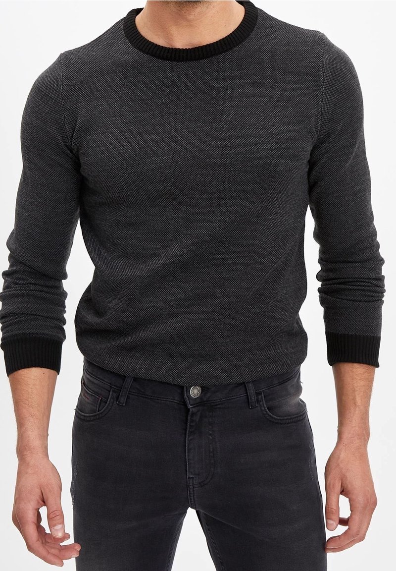 Homme portant un pull ajusté gris foncé texturé avec un col et des poignets côtelés noirs, associé à un jean en denim noir.
