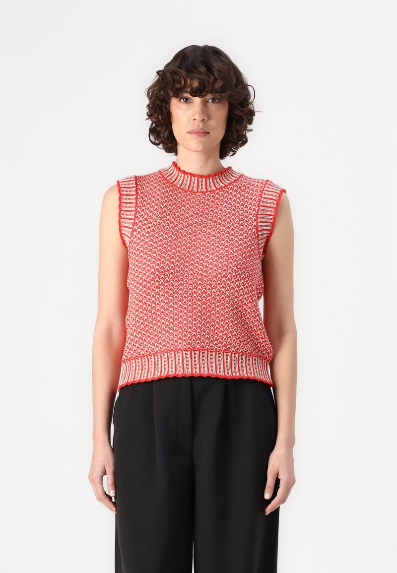 Rotes gestricktes ärmelloses Oberteil mit einem strukturierten Muster, geripptem Ausschnitt und Saum mit kontrastierenden Akzenten. Kombiniert mit schwarzen Hosen.