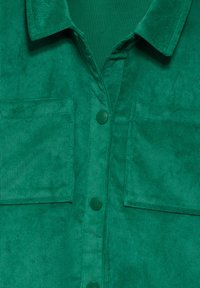 Grønne corduroy skjorte med krave, der har to påsyede lommer og grønne knapper. Teksturen er ribbet og blød, med en ensartet farve.