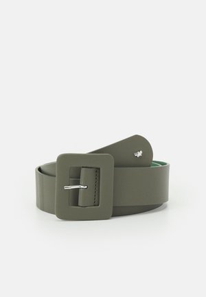 Olijfgroene brede riem met een grote vierkante gesp en een klein zilveren vlinderdetail vlak bij het uiteinde, opgerold afgebeeld op een witte achtergrond.