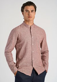 Camicia rossa a fantasia con colletto alla coreana, dotata di taschino sul petto e maniche lunghe, indossata da un modello su uno sfondo chiaro.