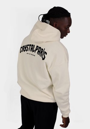 Cremefarbener Hoodie mit Kordelzug und großer schwarzer Schrift auf dem Rücken mit den Worten "CRYSTAL PARIS" und "KÄMPFE FÜR FREIHEIT." Weicher Stoff und lässige Passform.