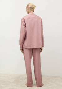 Rosa bomulljacka och matchande byxor, löst sittande med klassisk krage, bakfickor och synliga sömmar. Mjuk textur.