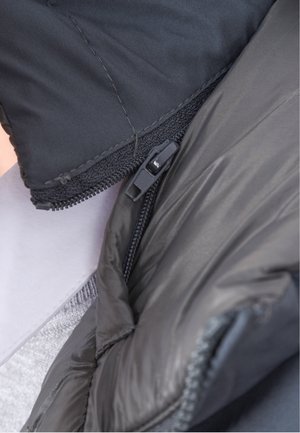 Giacca a vento nera in tessuto lucido, con zip dalla finitura liscia e cuciture visibili sulle cuciture.