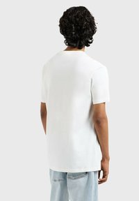 Camiseta blanca de manga corta hecha de un tejido suave, cuenta con un cuello redondo y un corte relajado. La vista trasera muestra un dobladillo recto y un diseño minimalista.
