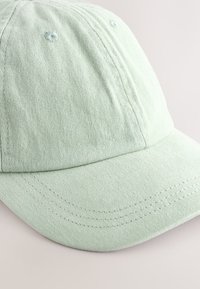 Cappellino da baseball verde chiaro in cotone, con visiera curva, design a sei pannelli e cuciture visibili sulla visiera e sui pannelli. Texture morbida.
