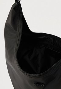 Svart nylon skulderveske med glatt tekstur, med glidelåsåpning og en liten logo foran. Interiøret er foret med svart stoff.