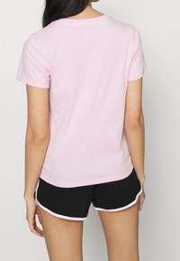 Růžové bavlněné tričko s kulatým výstřihem a krátkými rukávy. Hladká textura a mírně přiléhavý střih, nošeno s černými šortkami s bílým lemováním.