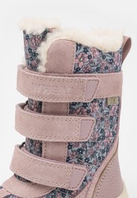 Rozā ūdensizturīga zābaku ar ziedu rakstu audumu, zamšādas akcentiem, mīkstu mākslīgu kažokādu odere un trim regulējamiem Velcro siksnām.