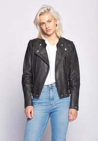 Sort læder bikerjakke med asymmetrisk lynlås, ribbede skulderdetaljer og lange ærmer. Båret over en hvid v-hals t-shirt.