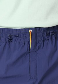 Navy blue shorts made of lightweight fabric with an elastic waistband, featuring a drawstring and a zippered pocket with a colorful accent.