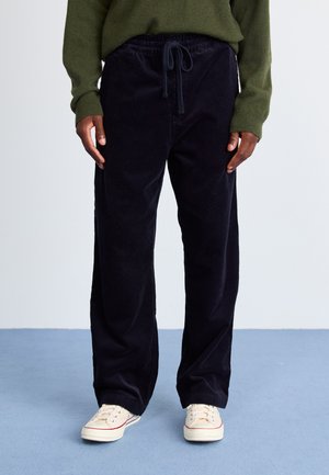 Navy corduroy pants with a drawstring waist, straight fit, and visible ribbed texture, paired with beige sneakers.