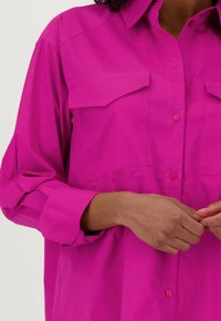 Felroze overhemdd met een kraag, twee borstzakken en opgerolde mouwen. Gemaakt van een soepel, lichtgewicht stof.