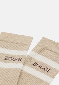 Calcetines a rayas en tonos beige y blanco con una textura acanalada. "BOCCI" está bordado en marrón oscuro en un lado.