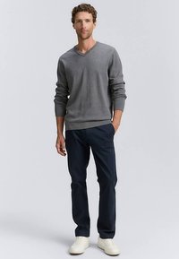 Pilkas V formos megztinis, tamsiai mėlynos kelnės ir balti sportbačiai. Megztinis turi ilgus rankovus ir laisvą siluetą, pagamintas iš minkštos mezginio medžiagos.