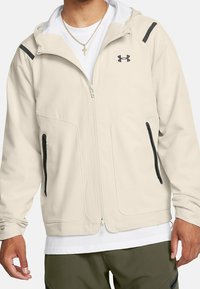 Beige zip-up jacka med huva, med svarta detaljer. Tillverkad av mjukt material, den har sidofickor och en figurnära design.