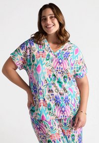 Camisa colorida de manga corta con cuello en V. Presenta un vibrante diseño floral y abstracto en rosa, verde, azul y púrpura sobre un fondo claro.