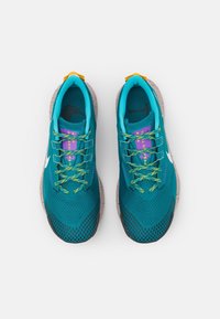 Teal træningssko med mesh-overdel, grønne og gule snørebånd, lilla detaljer og en spraglet beige sål. Har et hvidt logo på siden.