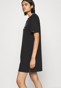 Svart oversized t-skjortekjole med korte ermer, med grafisk trykk foran og splitt på sidene i kanten for bedre bevegelse.