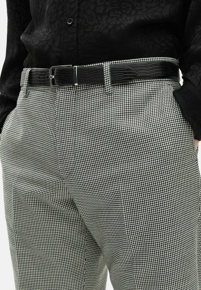 Pantalons à motif pied-de-poule noir et blanc avec une finition texturée, design ajusté, et une ceinture en cuir noir avec une boucle rectangulaire.