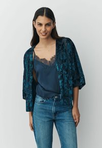 Dark teal, sheer kimono with floral pattern overlays, worn over a navy tank top with lace trim. Casual blue denim jeans complete the outfit.