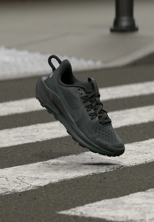 Zapatilla deportiva negra con parte superior de malla transpirable, superficie texturizada y suela de goma. Los cordones están bien ajustados y cuentan con una lengüeta.