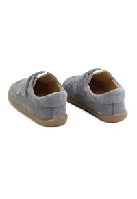 Zapatos de ante gris con un perfil bajo, punta redondeada y correas de velcro. Textura suave con una suela de goma para mayor tracción.