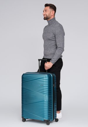 Valise rigide teal avec des rainures diagonales, poignée rétractable, quatre roues et fermeture éclair. Matériau léger et durable.