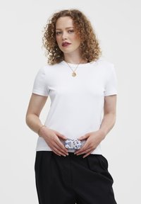 White short-sleeve t-shirt with a round neckline, paired with black trousers. A patterned belt bag is positioned at the waist.