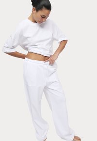 Weißes übergroßes T-Shirt aus Baumwolle und passende, locker sitzende Sweatpants mit elastischem Bund. Die Hose verfügt über eine Seitentasche.
