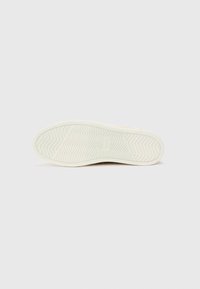 Suela de zapato de goma blanca con un patrón de tracción en zigzag, con el logo "TOMS" en relieve y bordes suaves, diseñada para ofrecer agarre y durabilidad.