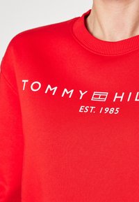Czerwona bluza bawełniana z okrągłym dekoltem, ściągaczami na rękawach i białym nadrukiem: "TOMMY HILFIGER EST. 1985."
